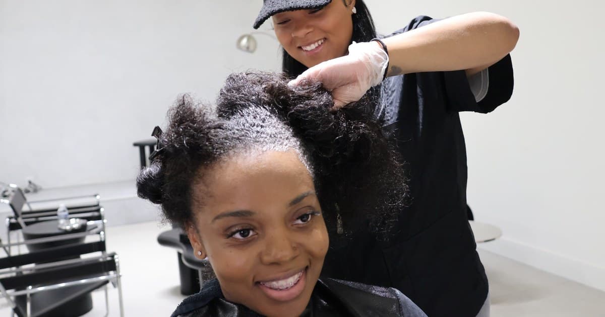 A smiling client looks toward the camera while her hairstylist works on her hair